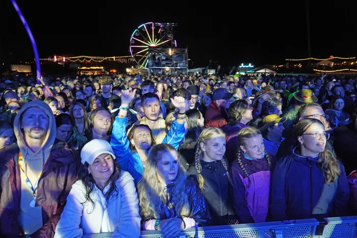 Eine große Menschenmenge bei einem nächtlichen Musikfestival mit einem beleuchteten Riesenrad im Hintergrund.