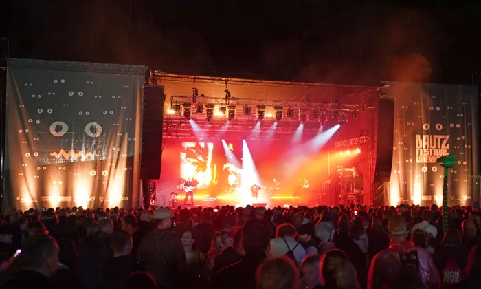 Die Band Alphaville tritt auf einer hell erleuchteten Bühne mit roter Beleuchtung vor einer großen Menschenmenge beim Bautz Festival auf.