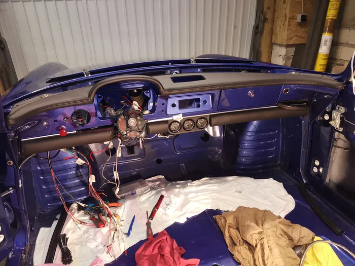 Das blaue Armaturenbrett eines Oldtimers während der Restaurierung mit freiliegender Verkabelung und Werkzeugen im Innenraum.