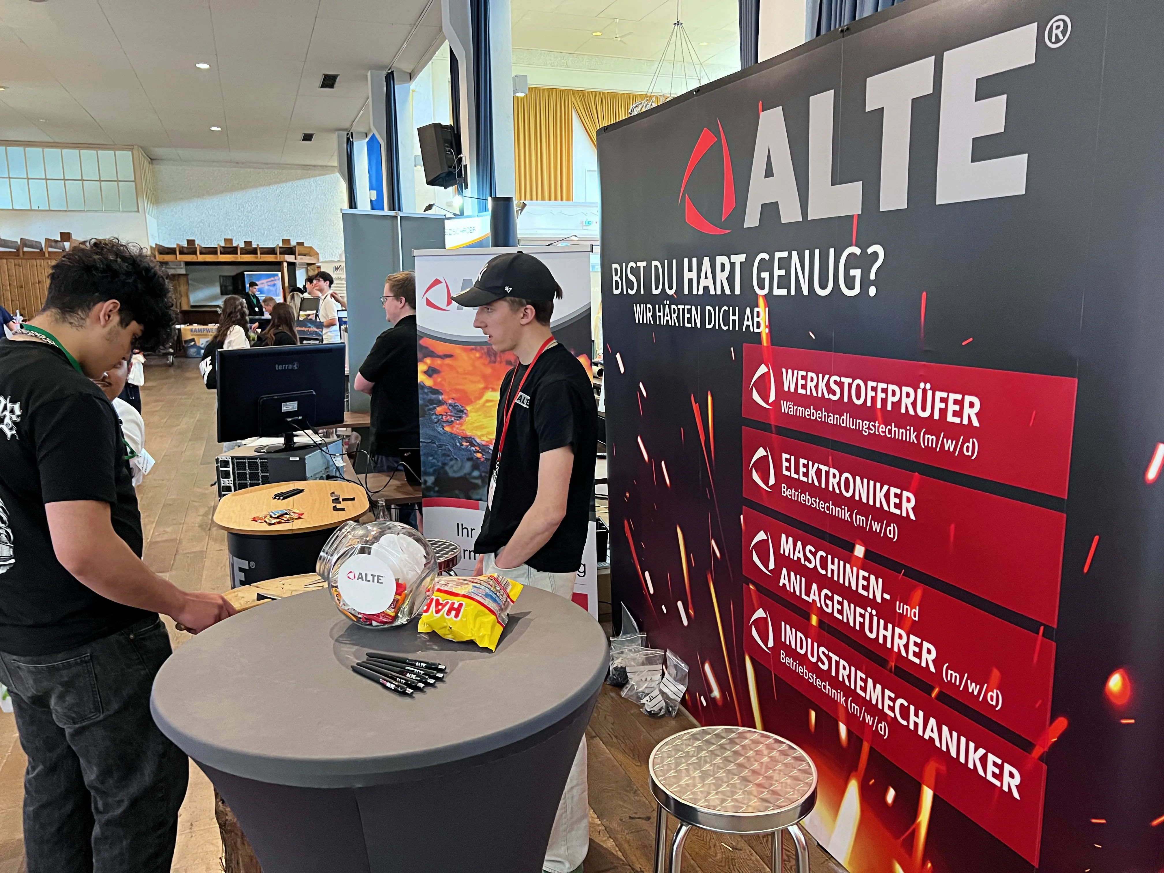 Stand von ALTE mit dem Slogan „Bist du hart genug?“, der Ausbildungsberufe wie Werkstoffprüfer und Elektroniker bewirbt. Im Vordergrund ein Mitarbeiter, der mit einem Besucher spricht.