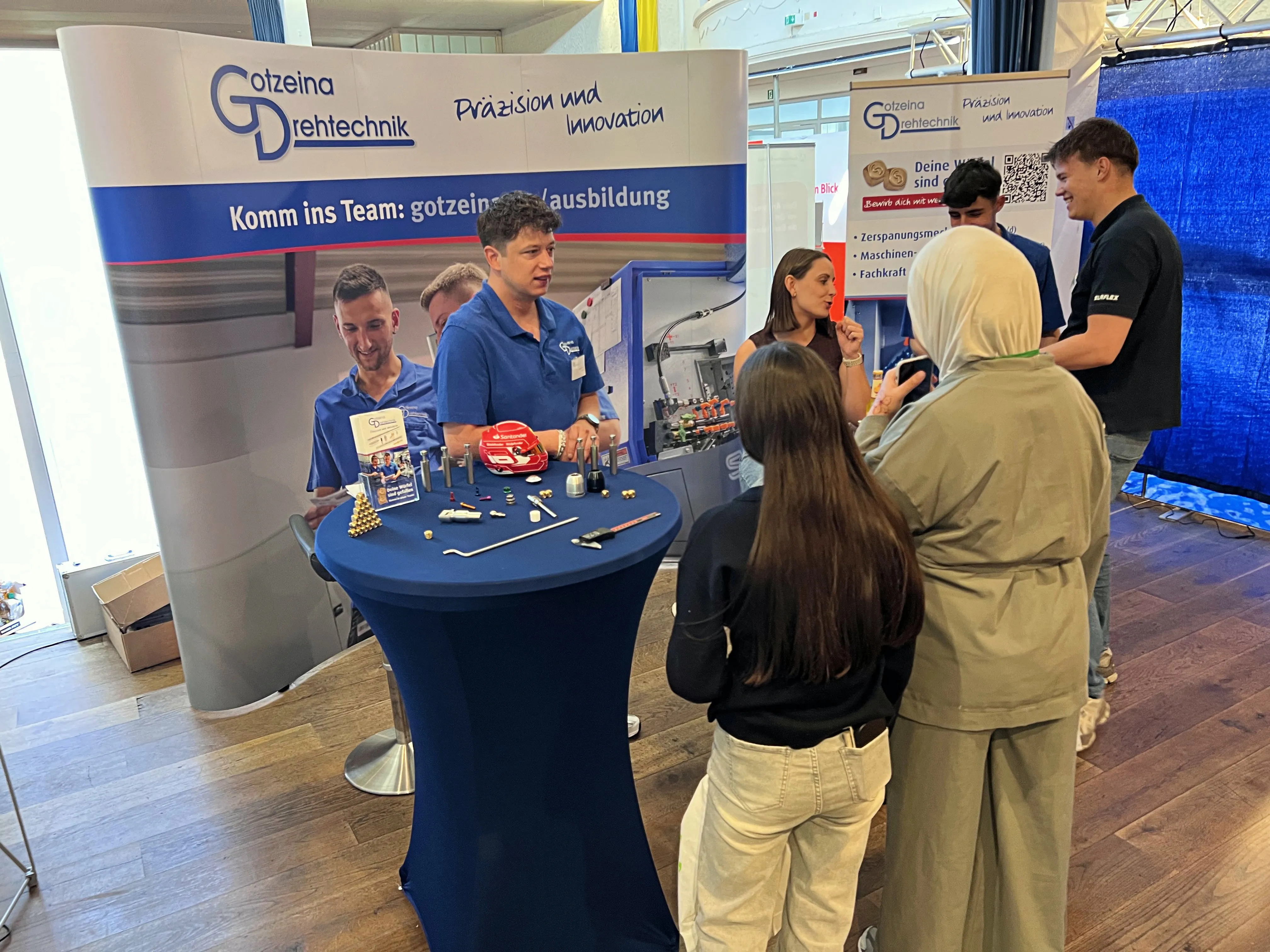 Mitarbeiter von Gotzeina Drehtechnik stehen an einem Messestand und beraten interessierte Besucher auf einer Ausbildungsbörse in Plettenberg.