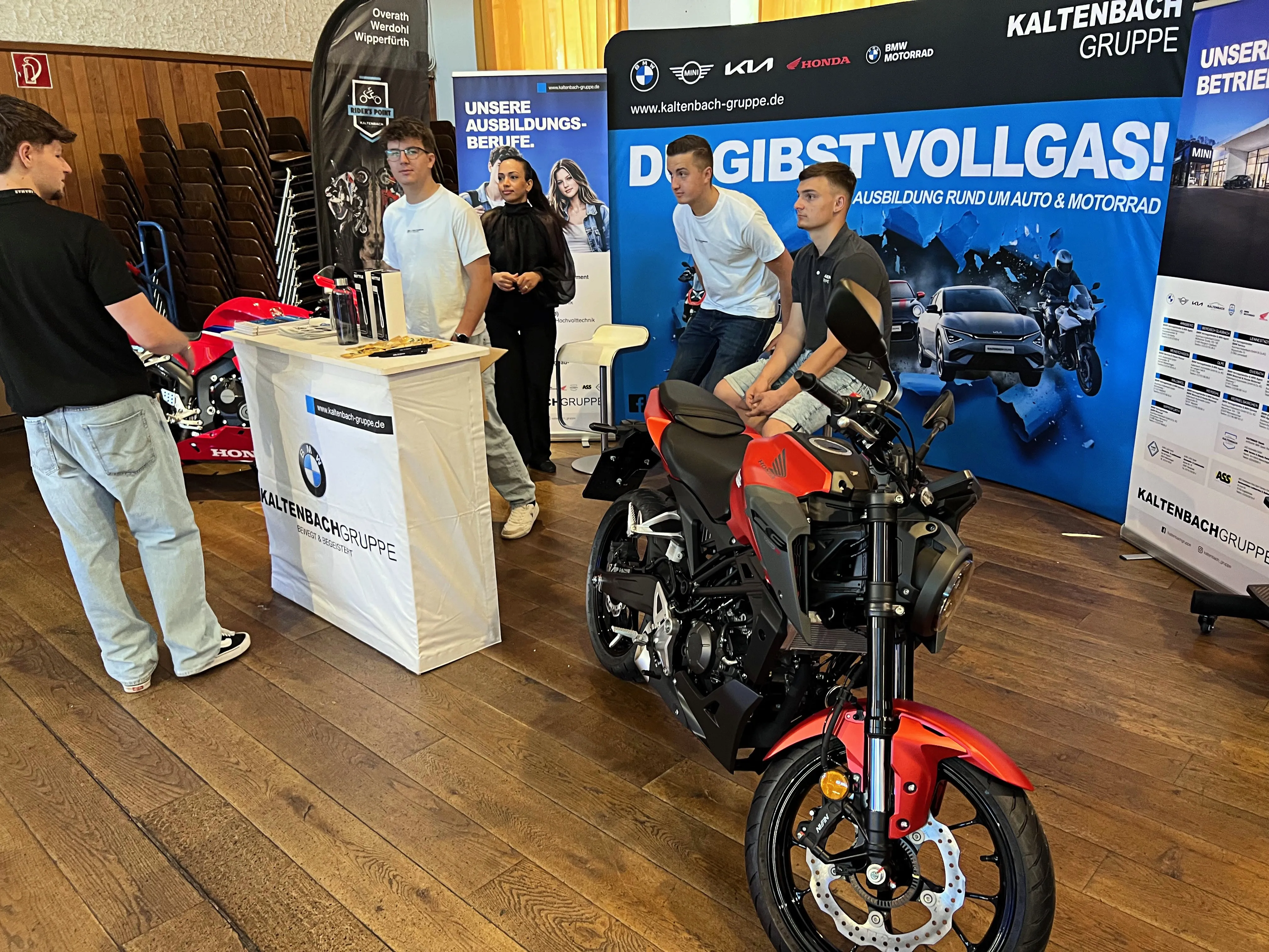 Motorrad auf einer Ausbildungsmesse in der Plettenberger Schützenhalle, im Hintergrund stehen Personen vor Infoständen.