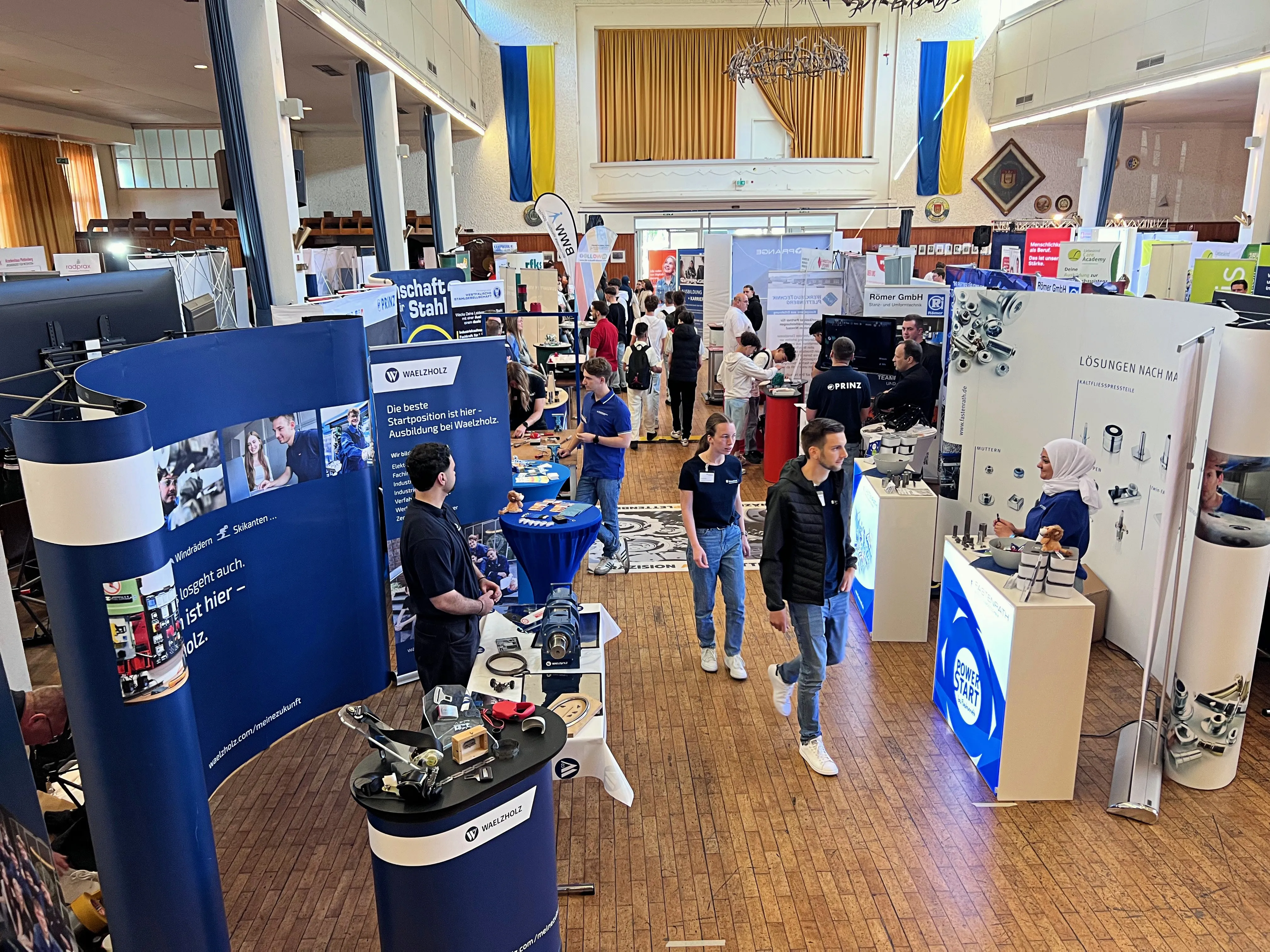 Blick über eine belebte Ausbildungsbörse in einer großen Halle mit zahlreichen Ständen und interessierten Besuchern.