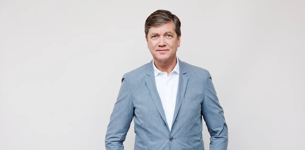 Porträt von Peter Prange, einem Mann mittleren Alters mit kurz geschnittenem, grau meliertem Haar, der einen blauen Anzug und ein helles Hemd trägt.