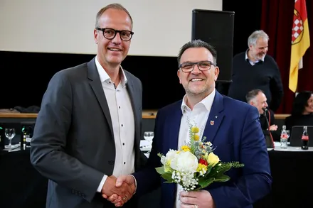 Axel Sippel und Bürgermeister Michael Joithe geben sich bei der Wiederbestellung Sippels zum Vorstandsmitglied der Sparkasse Iserlohn die Hände. Joithe überreicht Sippel einen Blumenstrauß.