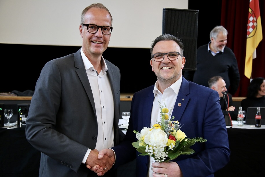 Axel Sippel und Bürgermeister Michael Joithe geben sich bei der Wiederbestellung Sippels zum Vorstandsmitglied der Sparkasse Iserlohn die Hände. Joithe überreicht Sippel einen Blumenstrauß.