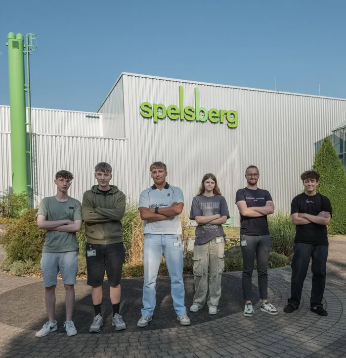 Sechs junge Auszubildende stehen in einer Reihe vor dem weißen Spelsberg-Firmengebäude.