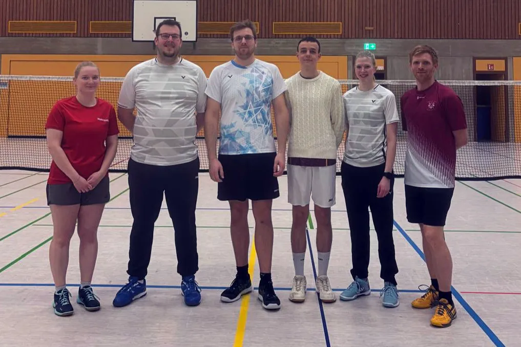 Fünf Badmintonspieler der 3. Mannschaft des BC Herscheid stehen in Sportkleidung auf einem Hallenboden vor einem Netz.
