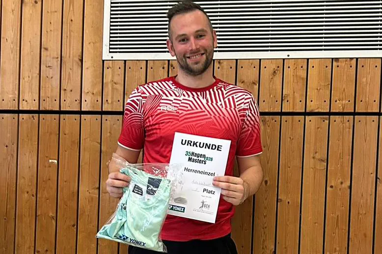 Ein Mann mit kurzem, blondem Haar hält eine Urkunde und ein Trikot in der Hand. Die Urkunde ist mit „Masters Herreneinzel“ und „35Hagen2026“ beschriftet.