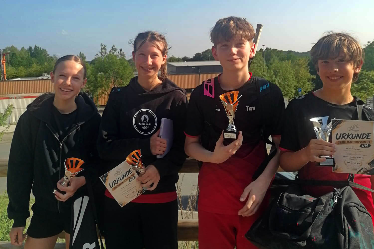 Vier junge Sportler*innen stehen mit Pokalen und Urkunden vor einer Sportanlage. Emilia und Sophie Baron, Tom Biehsmann und Julian Baron gewannen bei den Siegerlandmeisterschaften in Wenden.