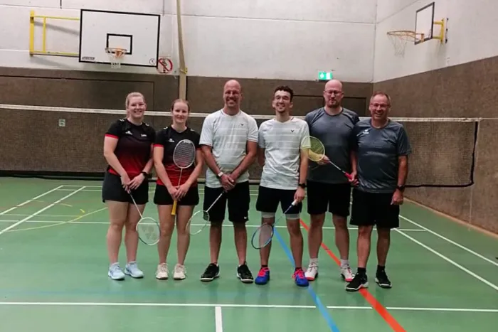 Sechs Mitglieder der 4. Herscheider Badmintonmannschaft stehen mit ihren Schlägern in einer Reihe auf einem Badmintonfeld in einer Sporthalle.
