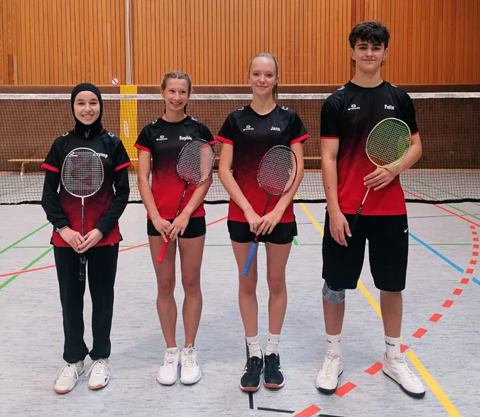 Vier Mitglieder der Herscheider U19 Badmintonmannschaft stehen in rot-schwarzer Sportkleidung mit Schlägern in einer Sporthalle.