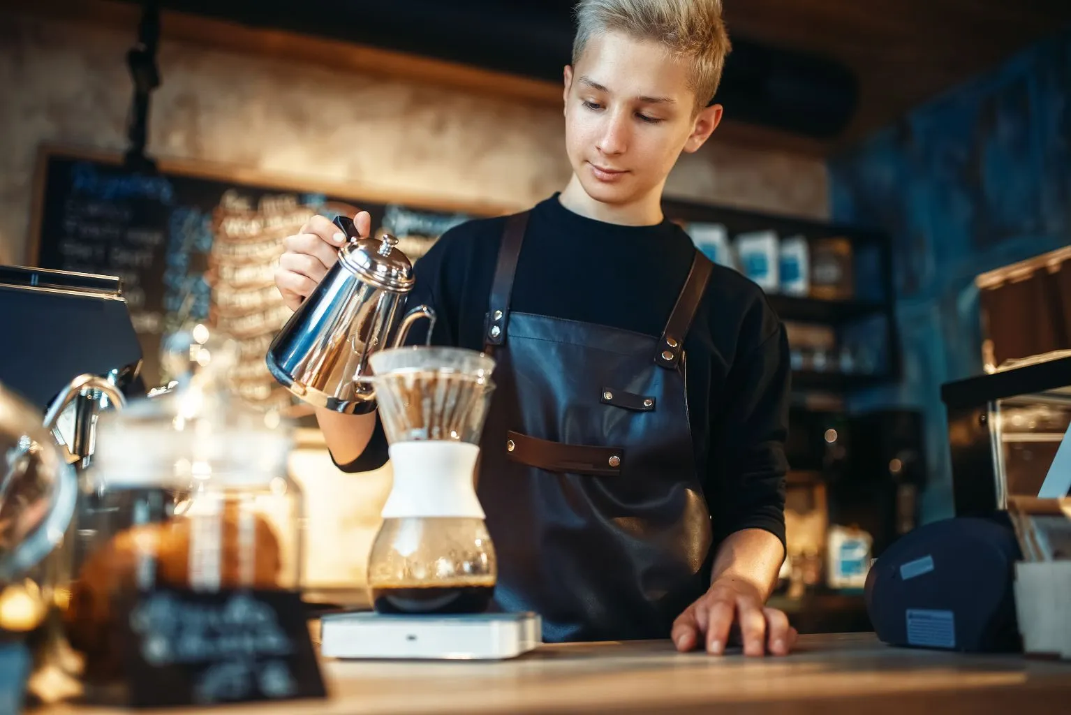 Junger Barista bereitet Filterkaffee zu, indem er Wasser über Kaffeepulver in einem Trichter gießt.