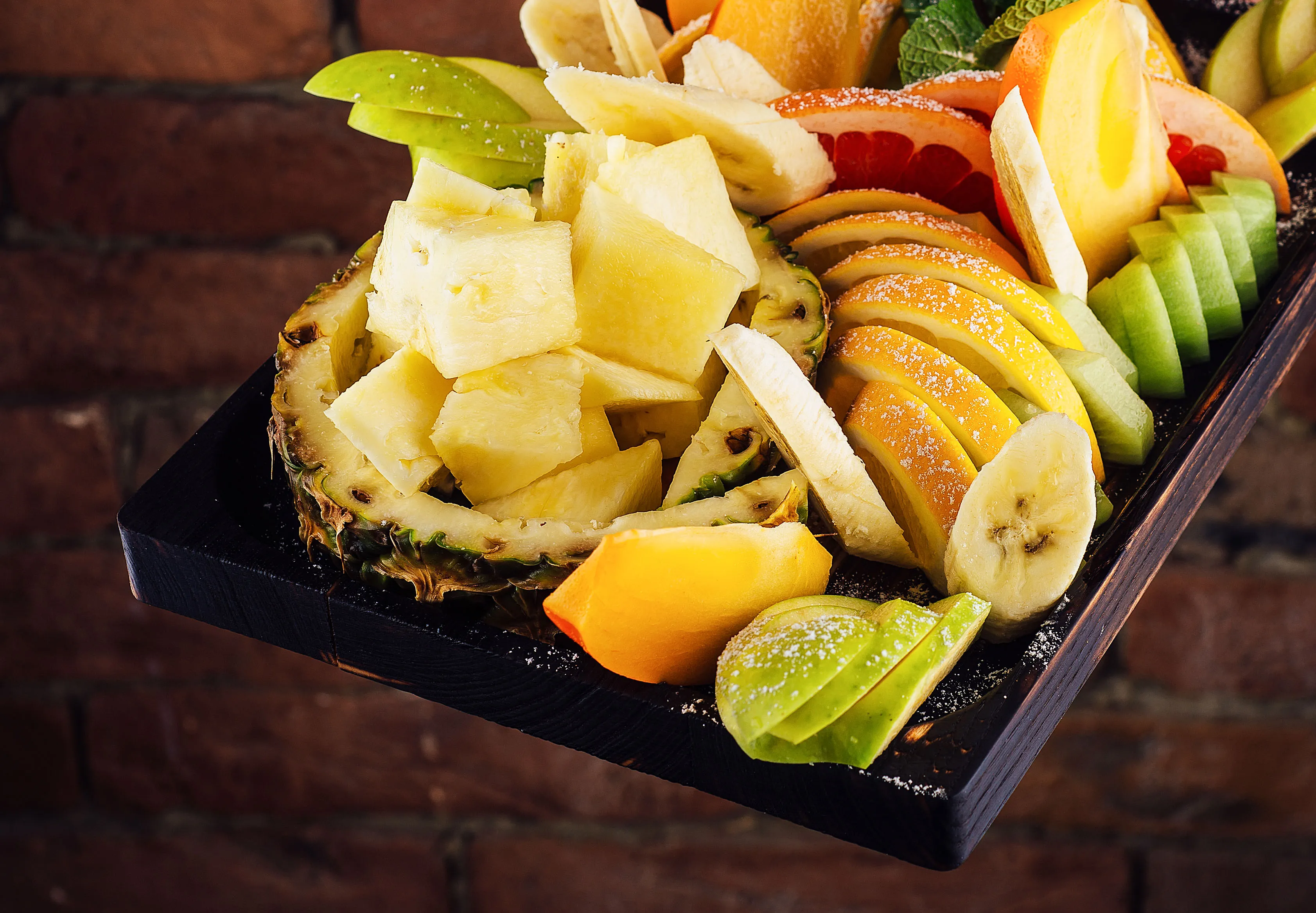 Obstsalat mit Ananas, Banane, Grapefruit und Apfel auf einer dunklen Holzplatte, möglicherweise zur Unterstützung der Lebergesundheit.