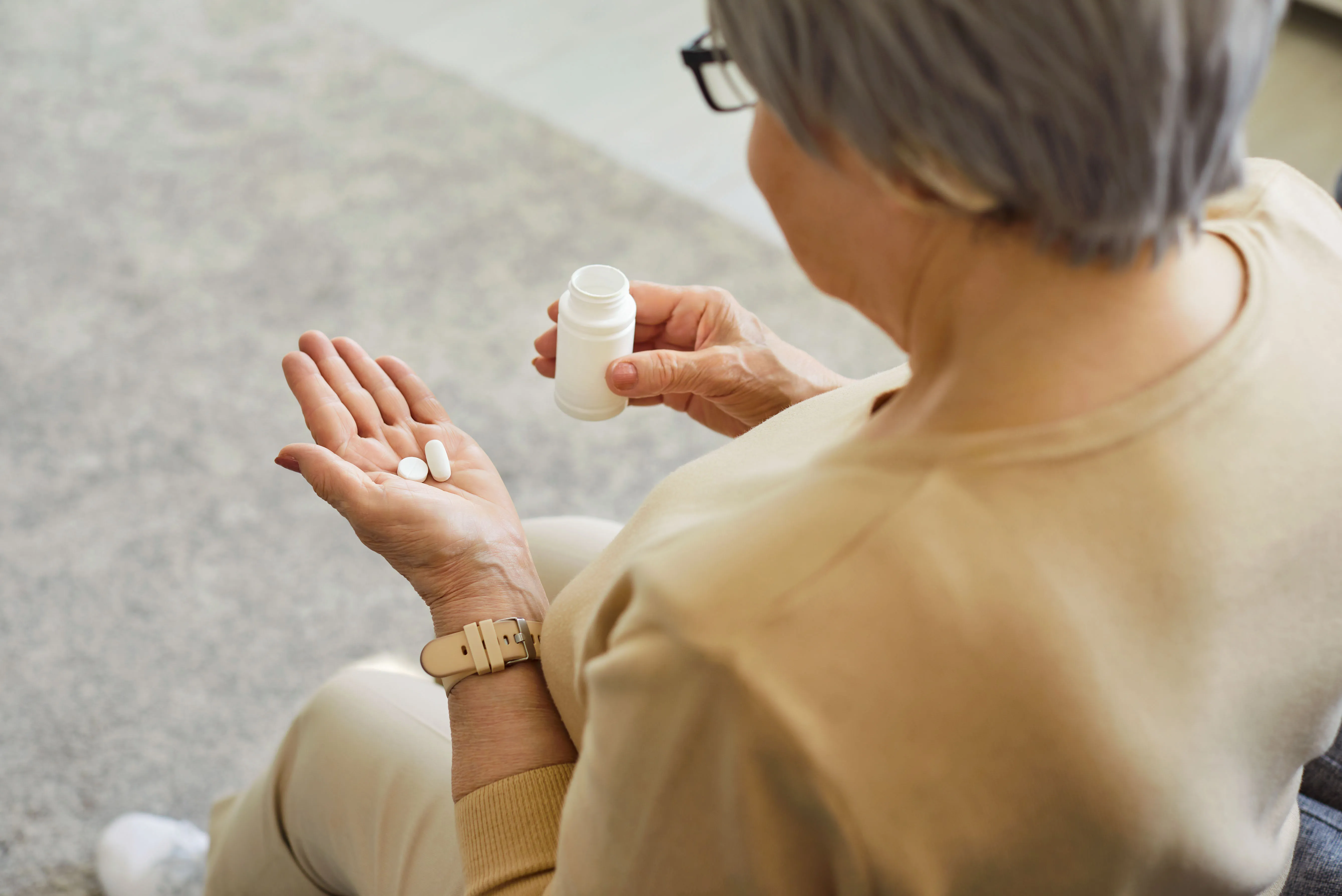 Eine ältere Person hält Tabletten in der Hand und eine Medikamentenpackung. Das Bild thematisiert das Risiko abgelaufener Medikamente.