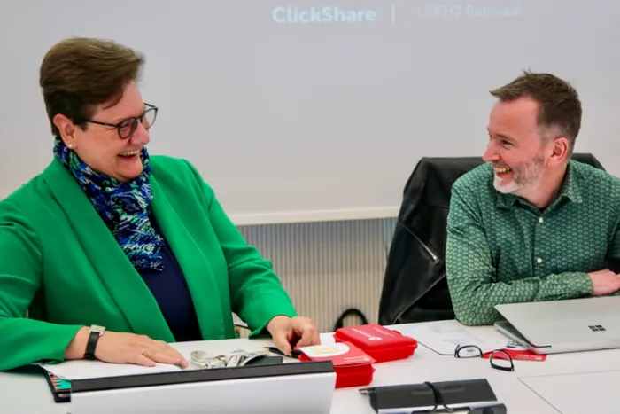 Zwei lächelnde Personen, Kreisdirektorin Barbara Dienstel-Kümper links und Ausschussvorsitzender Denis Potschin rechts, sitzen an einem Tisch und blicken auf Dokumente.