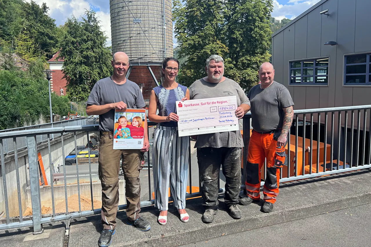Vier Männer stehen vor einem Silo und halten einen großen Scheck sowie ein Plakat.
