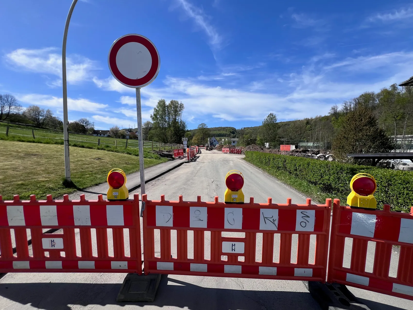 Eine gesperrte Straße mit Bauzäunen und Warnbaken. Im Hintergrund sind Bagger und Erdhaufen zu sehen.