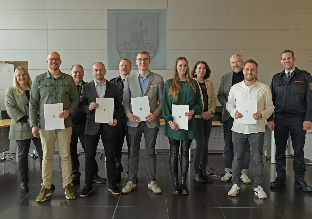 Neun Personen stehen in einer Reihe und halten jeweils ein Dokument in den Händen. Fünf davon sind die neuen Nachwuchskräfte der Feuerwehr Lüdenscheid.