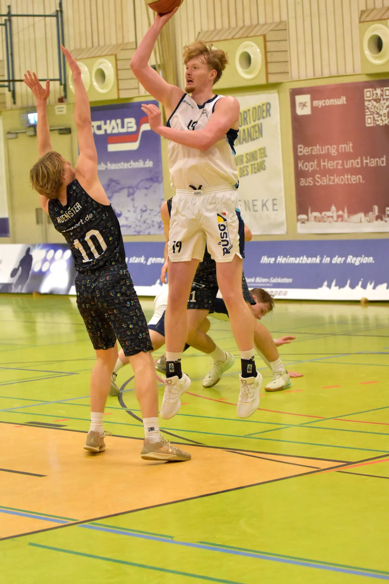 Basketballspieler Ben Luca mit dem Ball in der Luft, während er von Gegenspielern verteidigt wird.