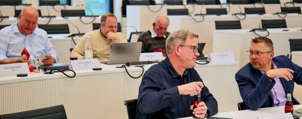 Fünf Männer sitzen an einem Konferenztisch und diskutieren. Namensschilder identifizieren sie als Mitglieder des Ausschusses für Abfallwirtschaft, Umweltschutz und Planung.