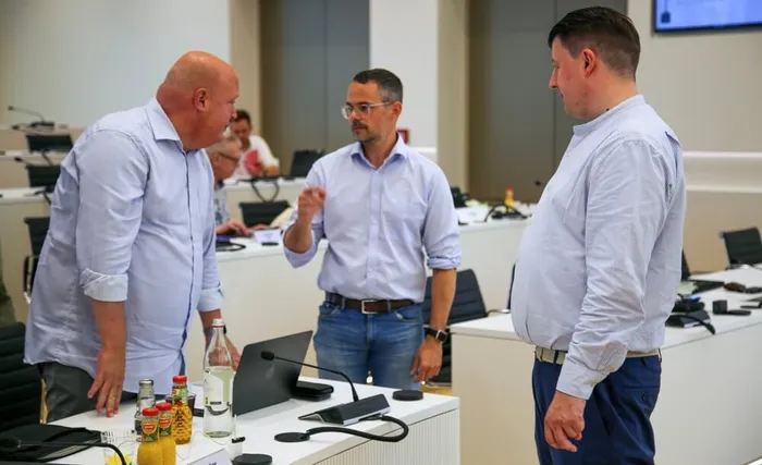 Drei Männer in Hemden stehen in einem Konferenzraum und unterhalten sich. Benjamin Friedrich und Fabian Ferber stehen sich zugewandt, während Kai Krause zwischen ihnen steht und gestikuliert.
