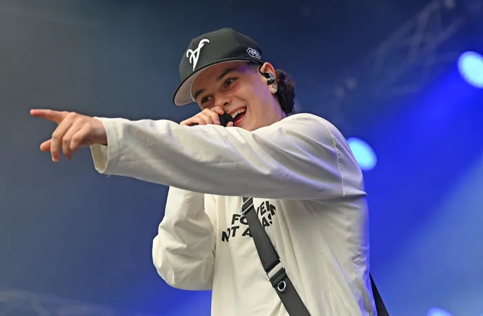 Benno singt in ein Mikrofon und zeigt mit ausgestrecktem Arm nach links auf einer blau beleuchteten Bühne.