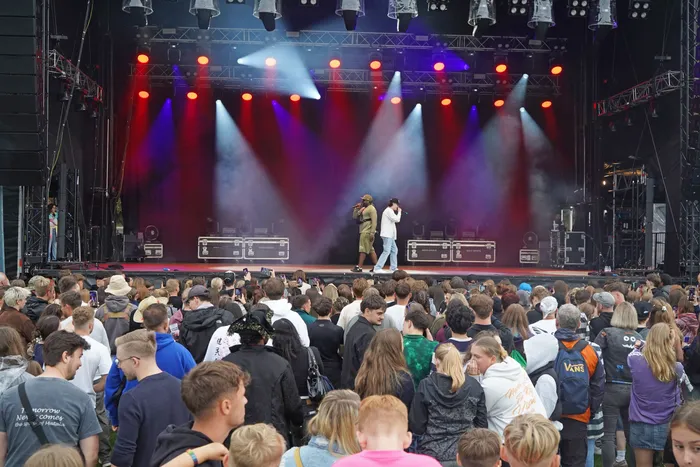 Zwei Musiker performen auf einer hell erleuchteten Bühne mit roten und blauen Scheinwerfern vor einer großen Menschenmenge.