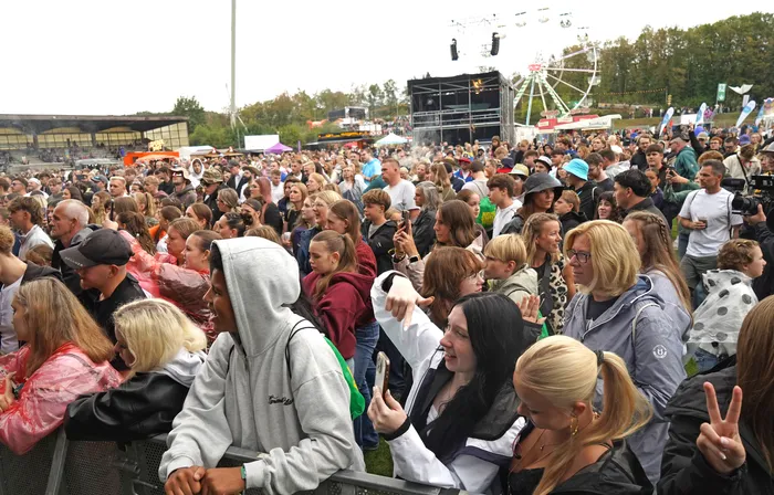 Eine große Menschenmenge bei einem Open-Air-Festival vor einer Bühne und einem Riesenrad.