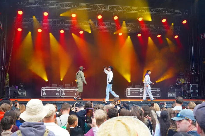 Musiker performen auf einer Bühne unter gelben und roten Scheinwerfern vor einem Publikum.