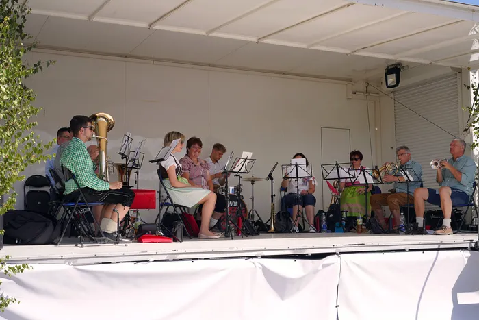 Eine Musikgruppe spielt mit Blasinstrumenten und Schlagzeug auf einer überdachten Bühne beim Bergfest der Löschgruppe Rärin.