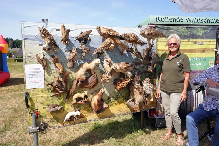 Eine Frau steht neben einer Ausstellungstafel mit verschiedenen präparierten Vögeln und Säugetieren vor einem Banner der „Rollenden Waldschule“.