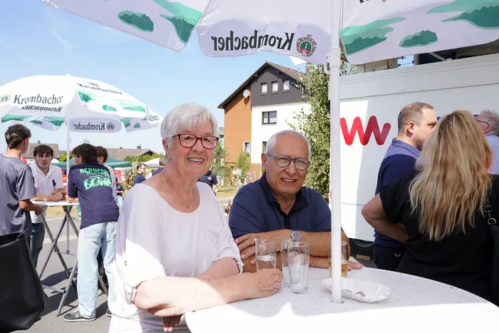 Eine Frau und ein Mann sitzen lächelnd an einem Tisch unter Krombacher-Sonnenschirmen bei einem Fest im Freien.
