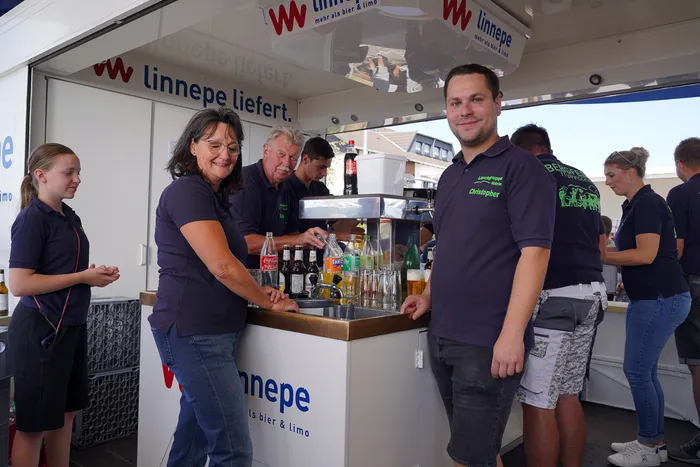 Mitarbeiter in dunkelblauen Poloshirts bedienen einen Getränkestand der Marke Linnepe beim Bergfest der Löschgruppe Rärin.