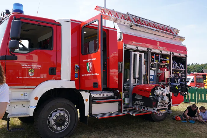 Ein rotes Feuerwehrfahrzeug mit geöffneten Geräteräumen, die technische Ausrüstung wie eine Pumpe und Schläuche zeigen.