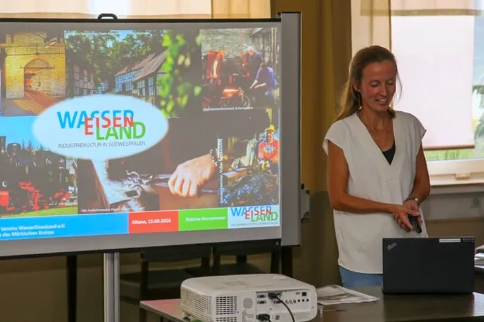 Bettina Hornemann steht neben einer Leinwand mit einer Präsentation zum Verein „WasserEisenLand“.