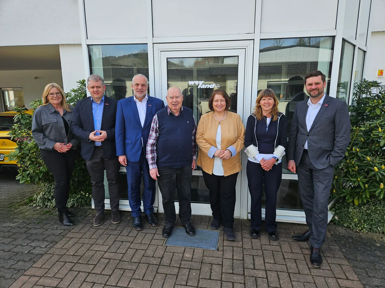 Gruppe von sieben Personen vor dem Eingang eines Gebäudes, darunter die Bundestagsabgeordnete Bettina Lugk.