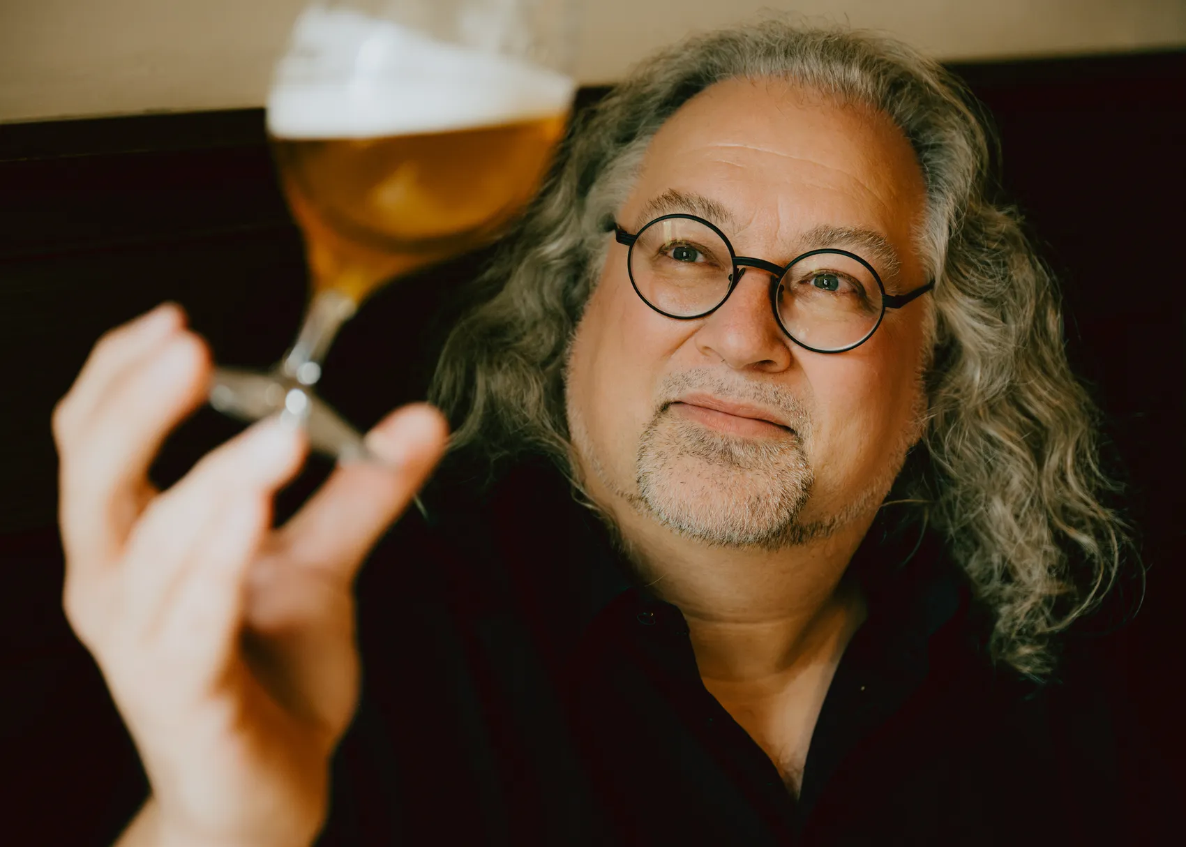 Markus Raupach, ein Mann mit grauen, lockigen Haaren und Brille, hält ein Bierglas vor sich.