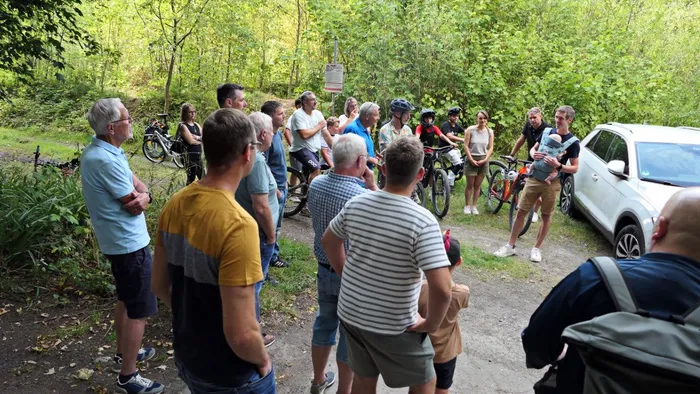 Eine Gruppe von Menschen mit Fahrrädern steht bei einem Treffen auf einem Waldweg in einem Waldgebiet.