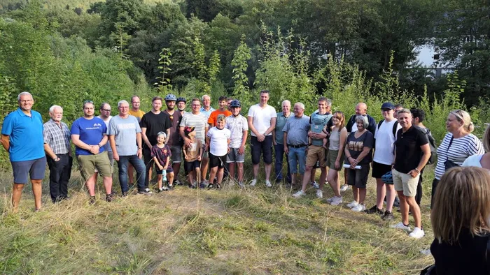 Eine Gruppe von Erwachsenen und Jugendlichen posiert für ein gemeinsames Foto auf einer Wiese vor einem Waldrand.
