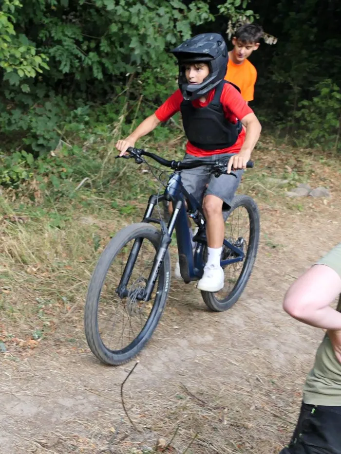Ein Junge mit schwarzem Helm, rotem T-Shirt und Schutzweste fährt auf einem blauen Mountainbike über einen unbefestigten Pfad.