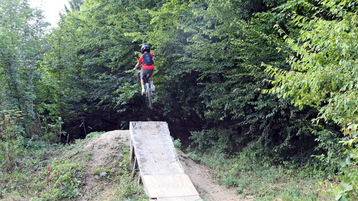 Ein Mountainbiker springt von einer Holzrampe in einem bewaldeten Bikepark.