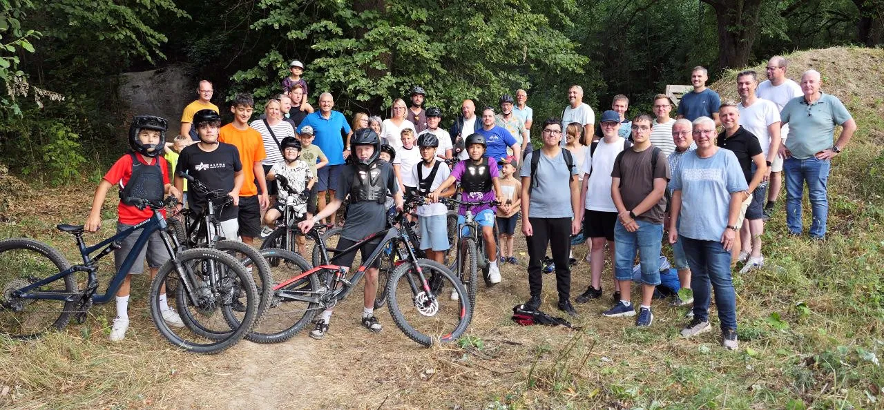 Eine Gruppe von Jugendlichen und Erwachsenen steht mit Mountainbikes auf einem Waldweg.