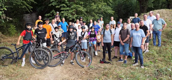 Eine Gruppe von Jugendlichen und Erwachsenen steht mit Mountainbikes auf einem Waldweg.