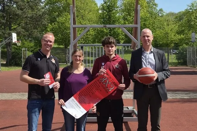 Vier Personen stehen auf einem Basketballplatz vor einem Korb und halten Werbematerial für ein 3x3-Basketballturnier der NRW-Tour in Iserlohn.