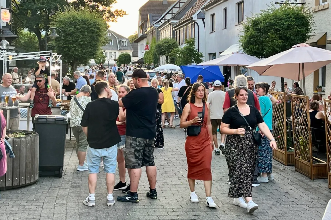 Menschen schlendern und sitzen vor Geschäften und Cafés in einer belebten Fußgängerzone während der Museumsnacht Breckerfeld.