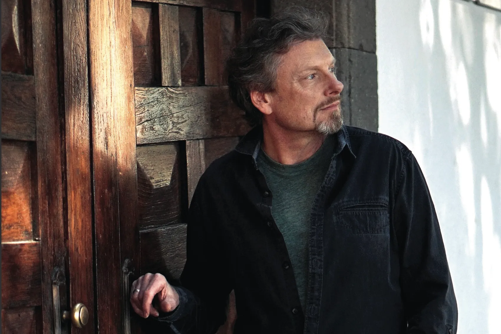 Porträt von Albert Frey, einem Mann mit graumeliertem Haar und Bart, der an einer Holztür lehnt und nachdenklich in die Ferne blickt.