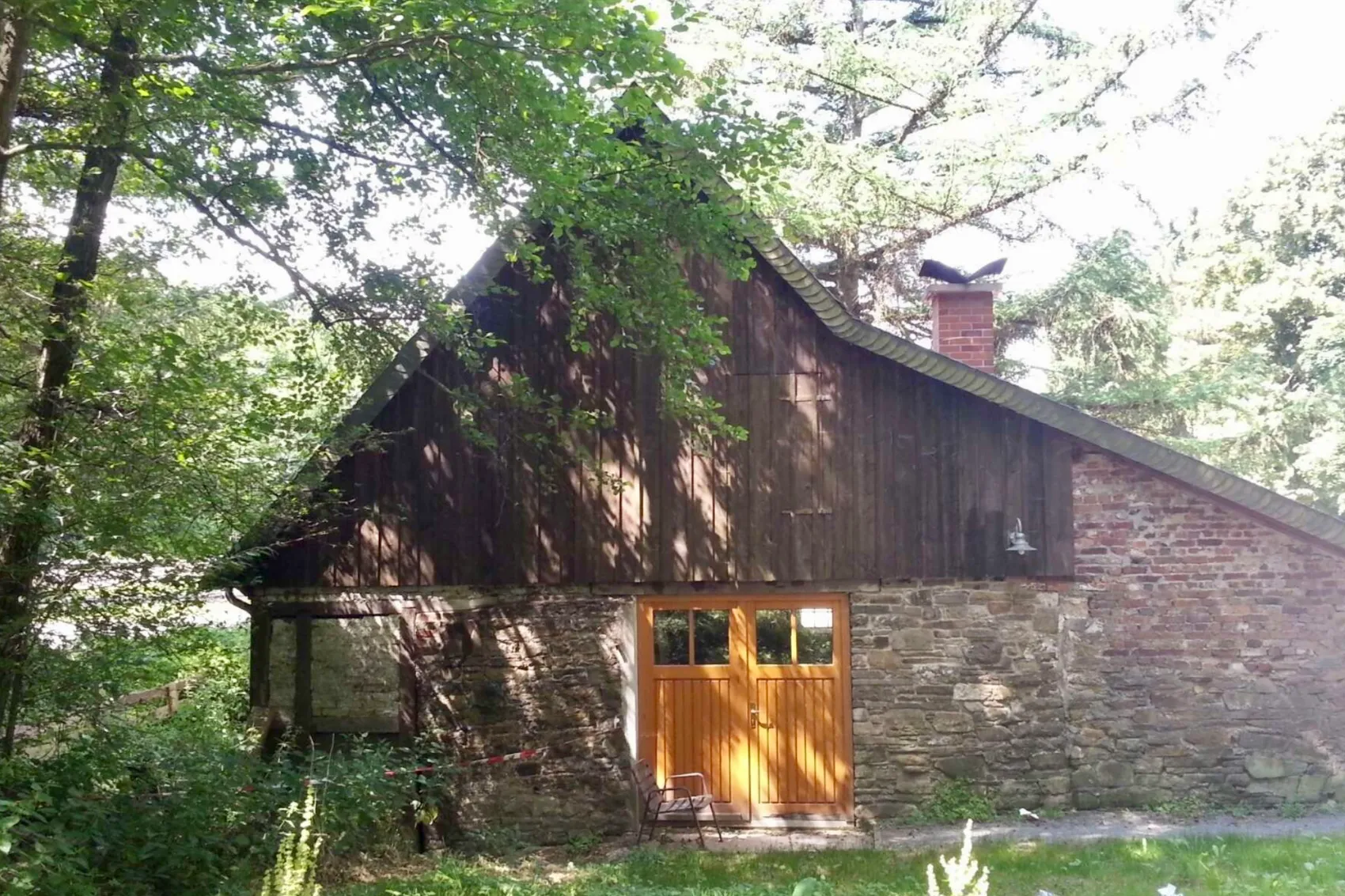 Rustikales Gebäude der Rhader Mühle mit Steinfassade und Holzelementen, davor eine Bank.