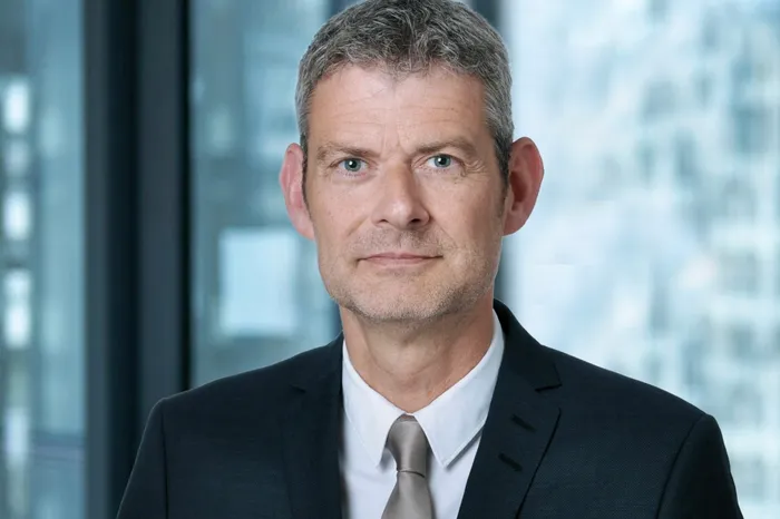 Niels-Erik Zumbaum, ein Mann mittleren Alters mit grauen Haaren, blickt in die Kamera. Er trägt einen dunklen Anzug mit Krawatte.