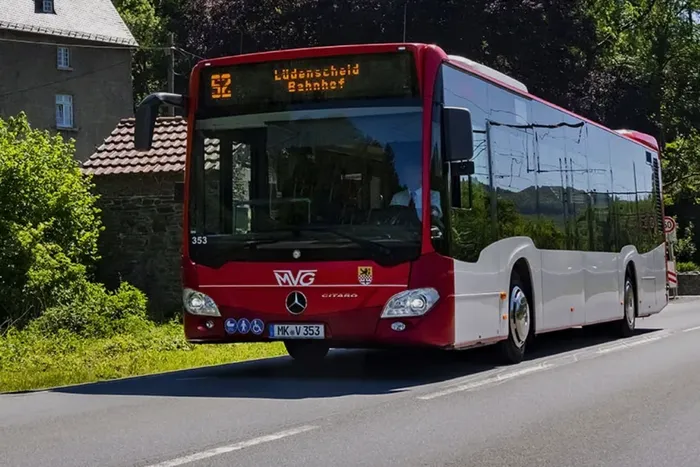 Ein rot-weißer MVG-Bus der Linie 52 mit der Zielanzeige „Lüdenscheid Bahnhof“ fährt auf einer Straße.